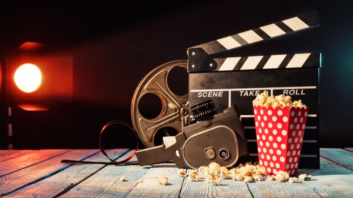 Kamera, filmový kotúč a popcorn na drevenom stole, symbolizujúci filmový priemysel.