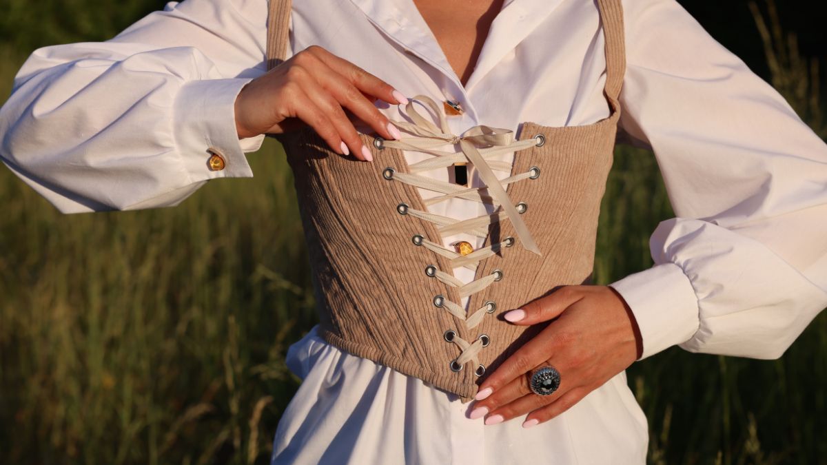 Žena v modernom korzete s bielou košeľou, ruky na šnurovaní korzetu.