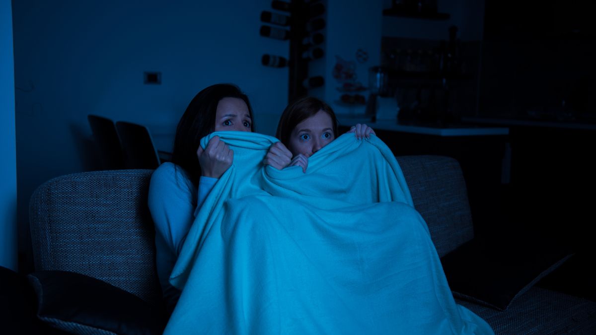 Dve osoby, matka a dcéra, s napätými výrazmi sledujú hororový film v tme.