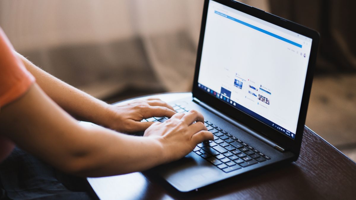 Osoba píše na laptop v domácom prostredí, zameraná na obrazovku.