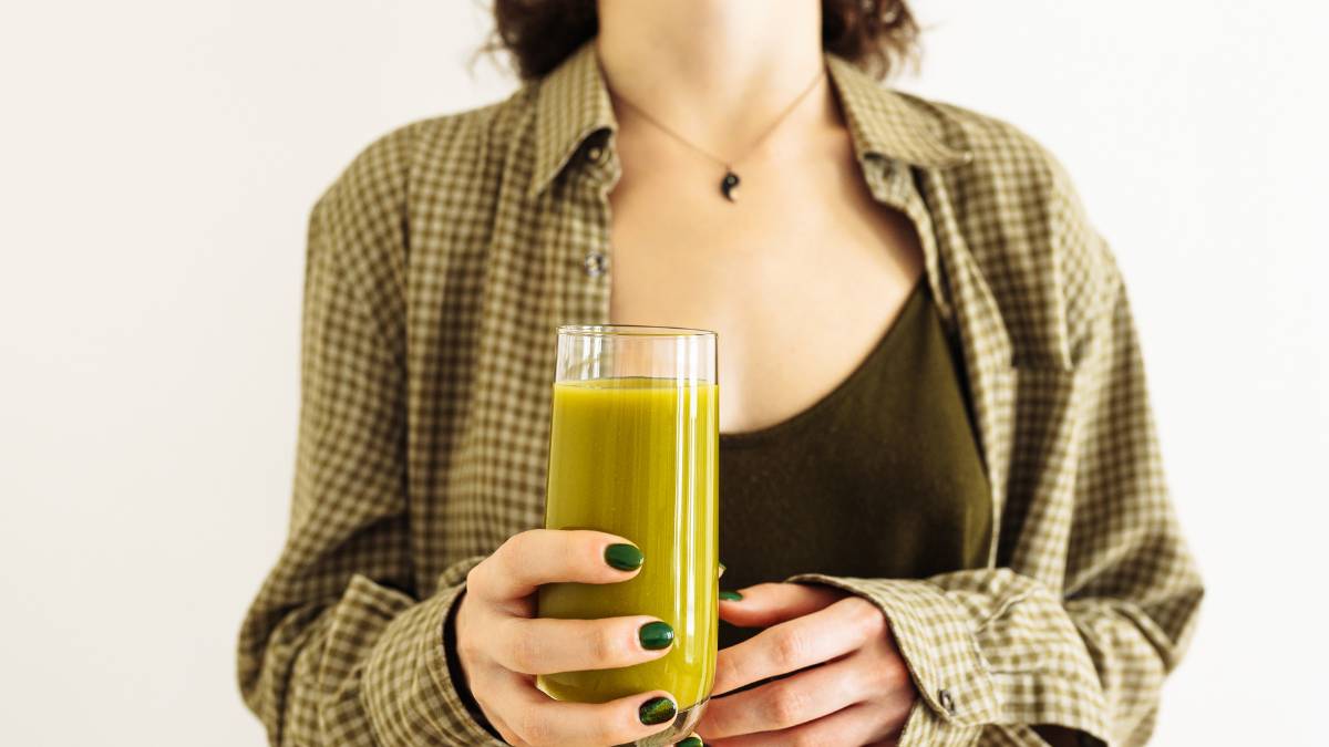 Žena drží pohár so zeleným smoothie, symbolizujúcim detoxikáciu a zdravú výživu.