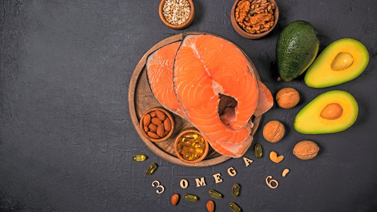 Na drevenej doske sú plátky lososa, avokádo, orechy a omega-3 kapsuly.