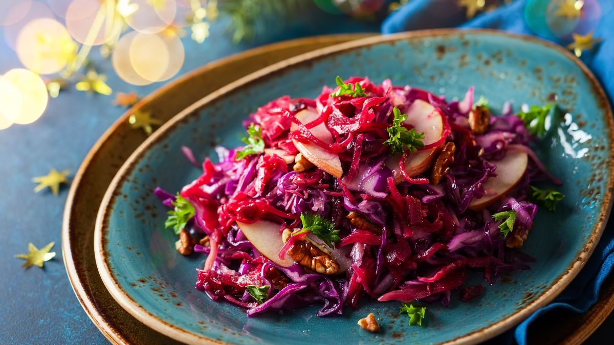 Miska s červenou kapustou, jablkami a orechmi na modrom pozadí.