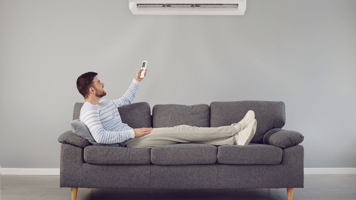 Muž relaxuje na pohovke a ovláda klimatizáciu diaľkovým ovládačom.