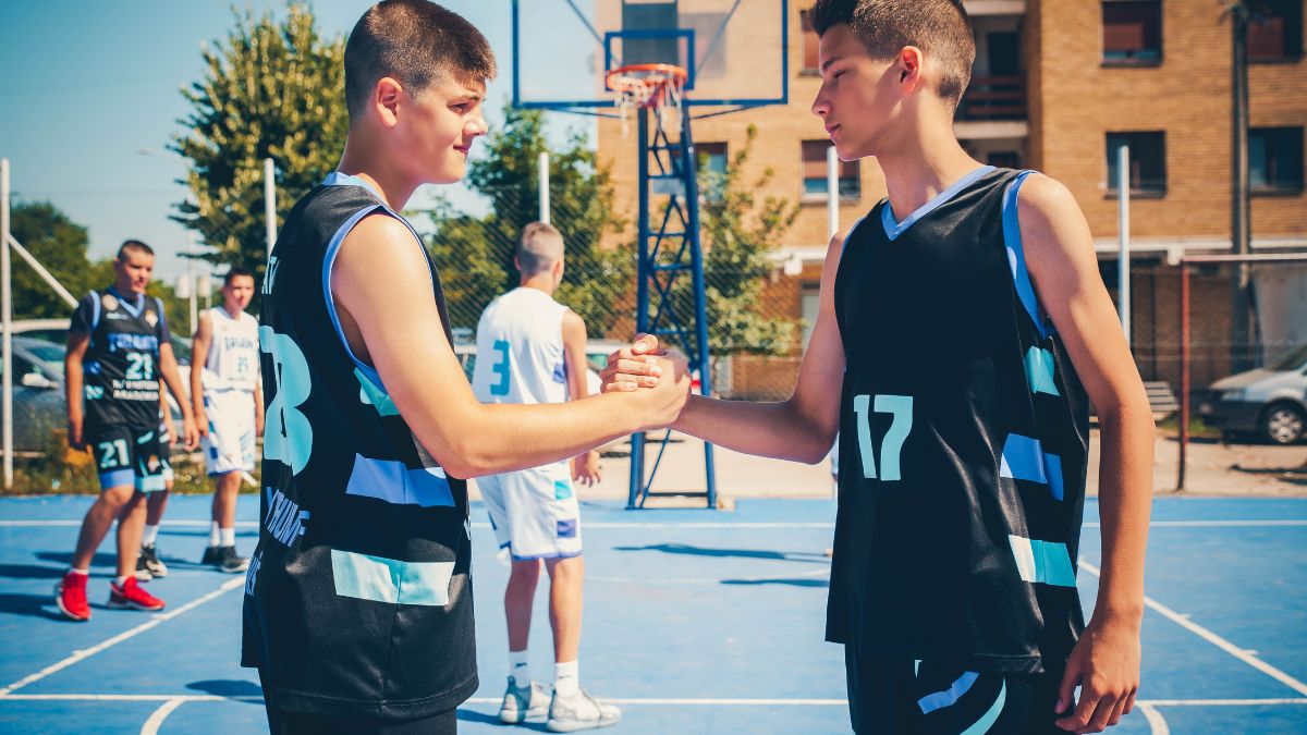 Dva chlapci v basketbalových dresoch si podávajú ruky na ihrisku.
