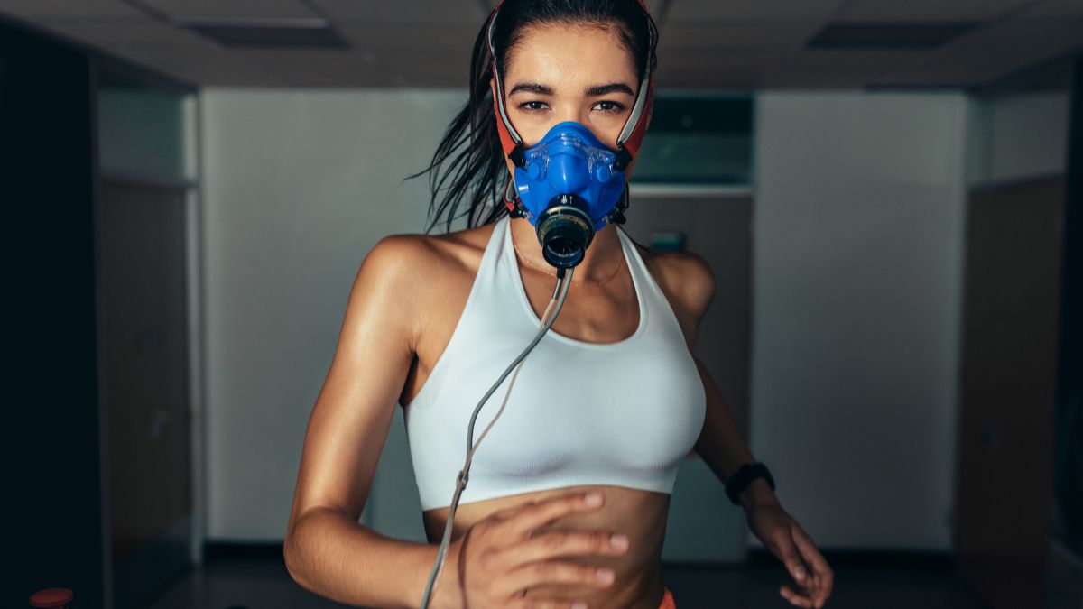 Žena v tréningovej maske beží na bežeckom páse v telocvični.
