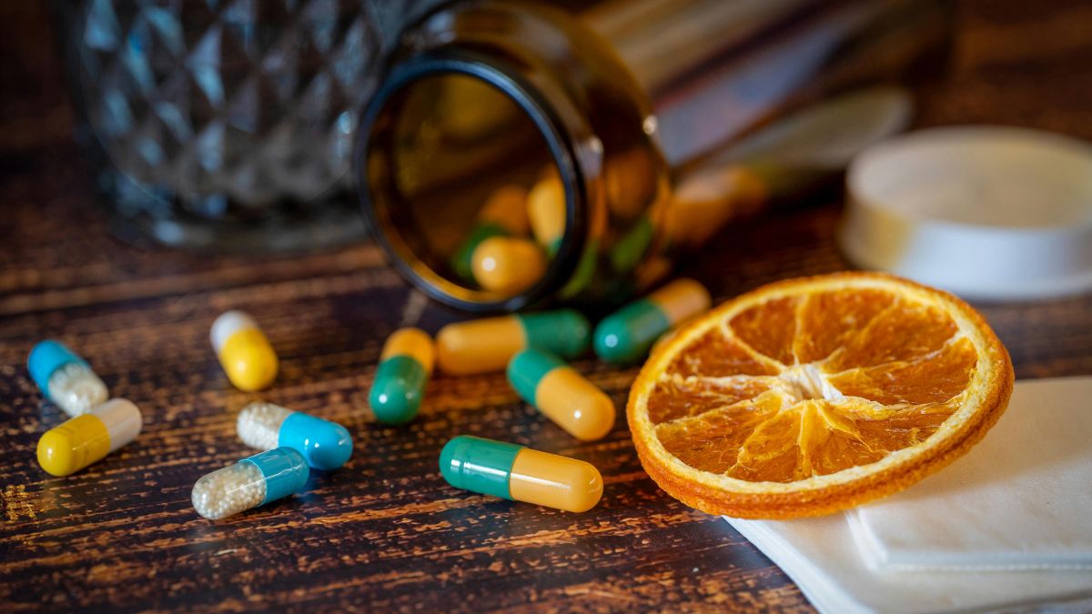 Rôzne vitamínové kapsuly a sušený pomaranč na drevenom stole.
