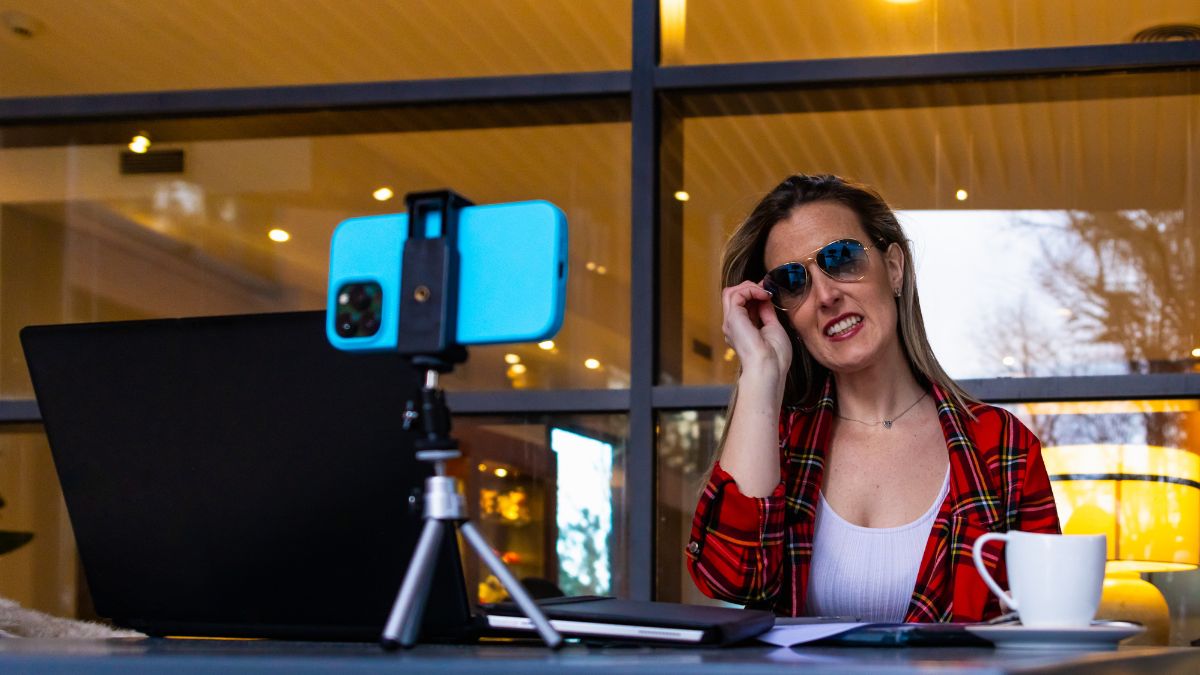 Žena v slnečných okuliaroch sedí pred laptopom a natáča video.