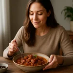 Žena vychutnávajúca si kohútí perkelt s pohárom šalátu vedľa