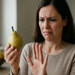 Žena s výrazom znechutenia pozerá na hrušku, potenciálne nebezpečenstvo.