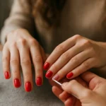 A woman receives a gel nail treatment with red polish.