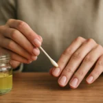 Žena aplikuje olej na nechty pomocou vatovej tyčinky.