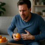 Muž s bolesťami brucha držiaci mandarínku